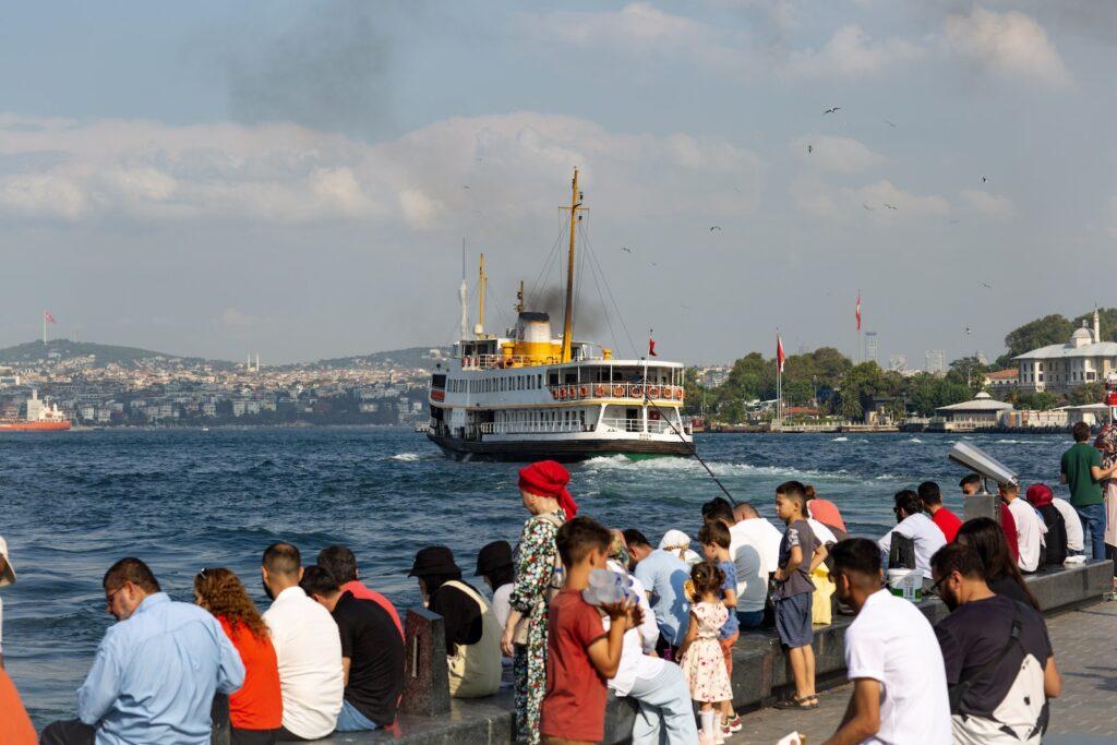 People Sitting on the Shore and Looking at a Passenger Ship Cruising in the Bosphorus Strait, Istanbul, Turkey